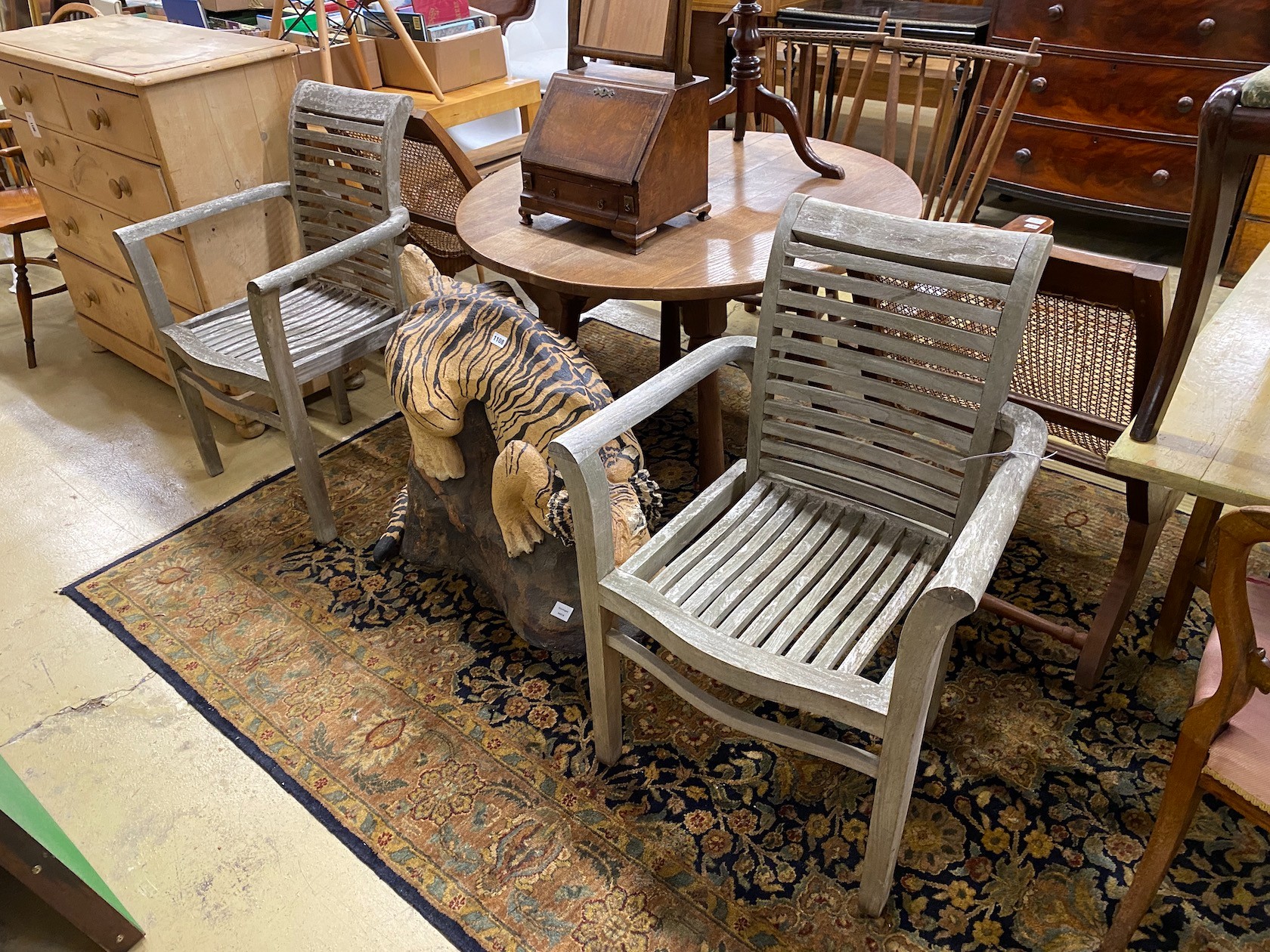 A pair of weathered teak slatted garden elbow chairs, width 65cm, depth 45cm, height 95cm